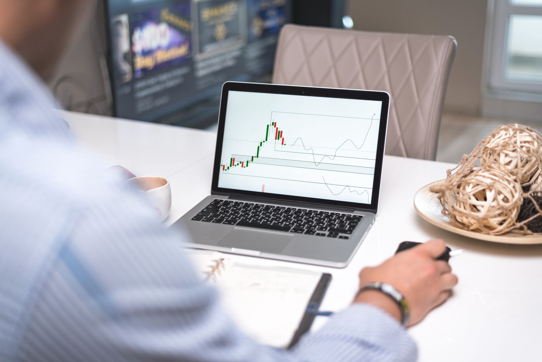 Un trader revisa la pantalla de un portátil junto a un diario manuscrito, en una imagen que ilustra los historiales de trading y las notas personales que utilizan las herramientas de análisis del comportamiento.