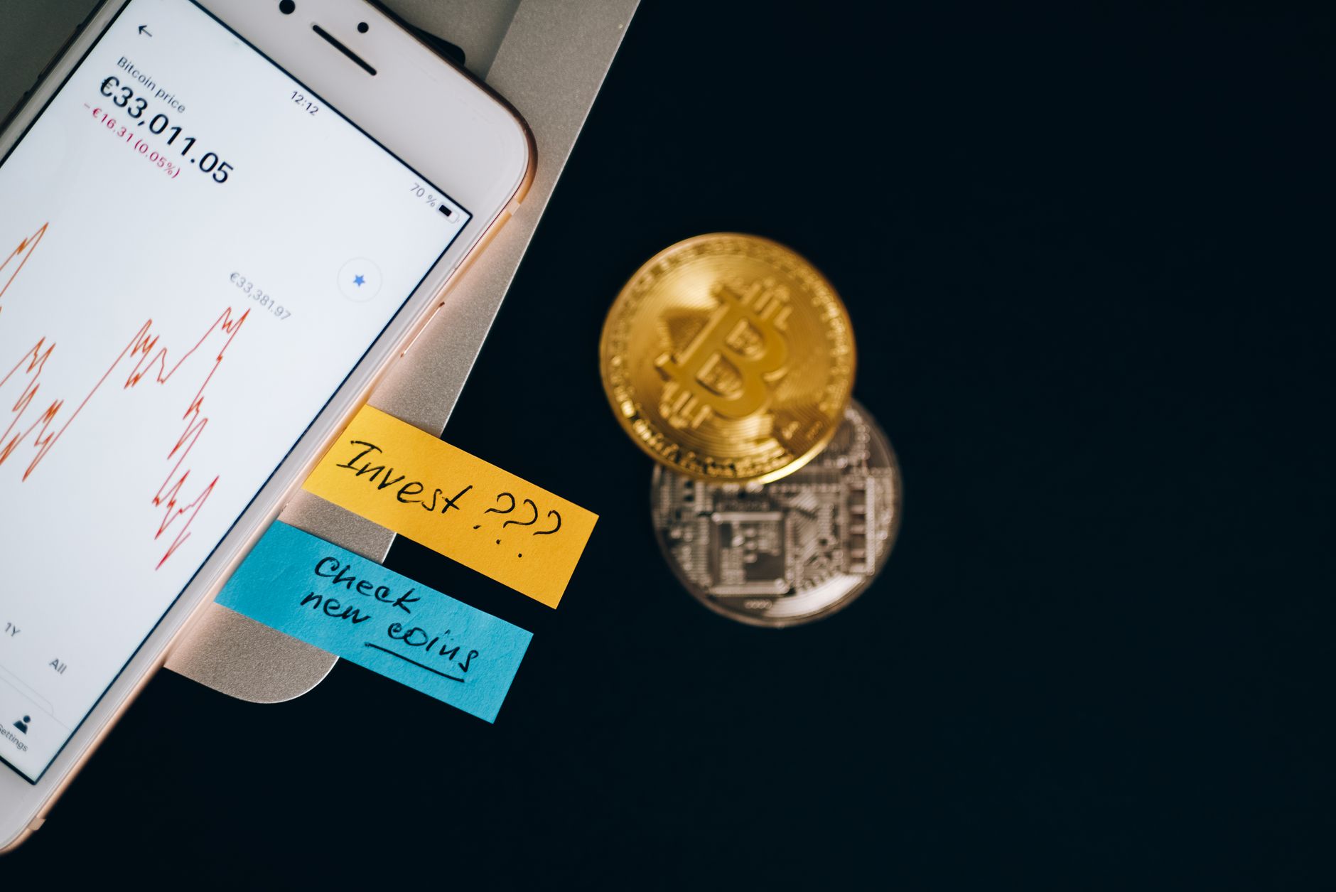 A smartphone beside a cryptocurrency coin, illustrating Ether staking access through a brokerage platform.